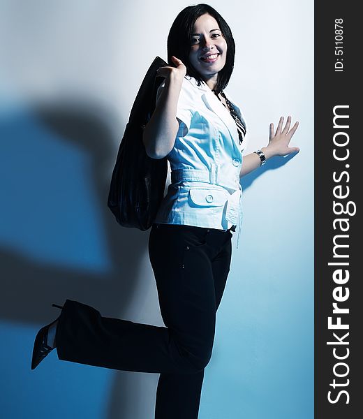A high-key portrait about a cute stylish woman with black hair who is lighted with blue, she is lifting up her leg and she has an attractive look. She is wearing black pants, a white coat and a stylish handbag. A high-key portrait about a cute stylish woman with black hair who is lighted with blue, she is lifting up her leg and she has an attractive look. She is wearing black pants, a white coat and a stylish handbag.