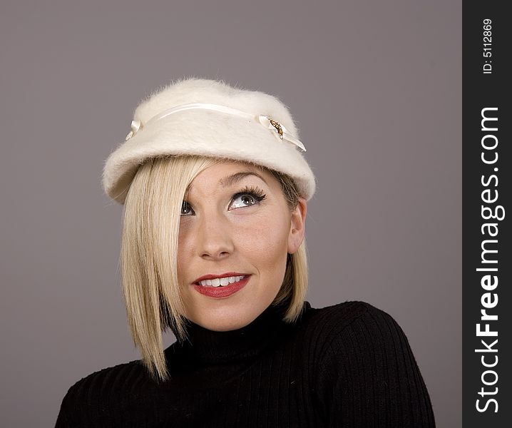 A blonde in a black turtleneck and a white fur hat looking up and to the left. A blonde in a black turtleneck and a white fur hat looking up and to the left.