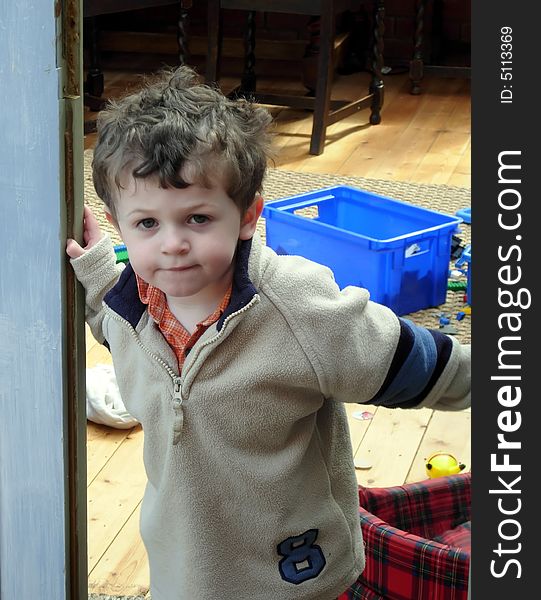 A thoughtful young child leans out of his playroom door. A thoughtful young child leans out of his playroom door.