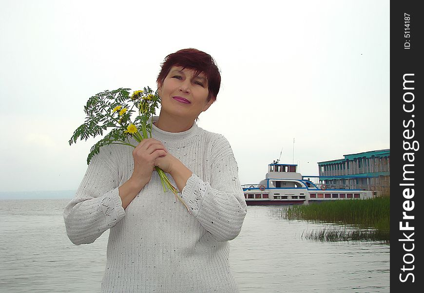 Trip to a province. Rural landscape. Happy business woman with the bouquet of the field flowers on a background of the river and excursion ship. Trip to a province. Rural landscape. Happy business woman with the bouquet of the field flowers on a background of the river and excursion ship.