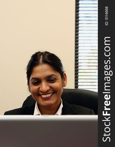 Indian businesswoman sitting behind her laptop with a huge smile on her face. Indian businesswoman sitting behind her laptop with a huge smile on her face