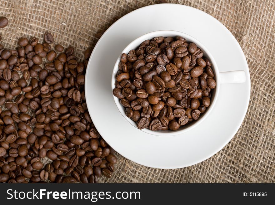 Cup with freshly roasted coffee beans on sackcloth. Focus on the cup.