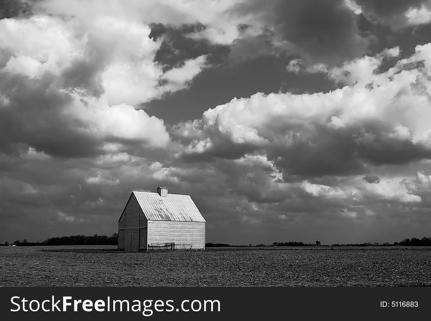 A small barn sits in the middle of a field, under a dramatic sky (black and white photo). A small barn sits in the middle of a field, under a dramatic sky (black and white photo).