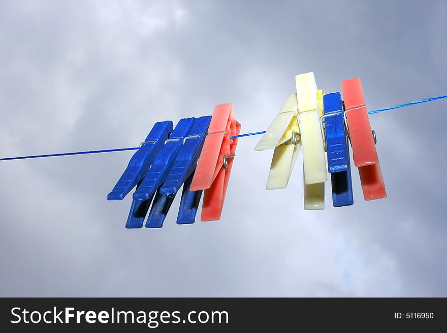 Colorful clothespins with rain drops on the rope on the sky background.