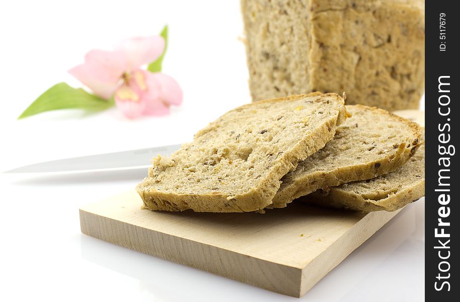 Fresh sliced whole grain bread on wooden board with knife, flower in the background. Fresh sliced whole grain bread on wooden board with knife, flower in the background