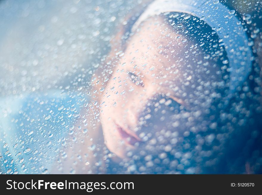 Young girl looking through window after rain. Focus on drops. Young girl looking through window after rain. Focus on drops.