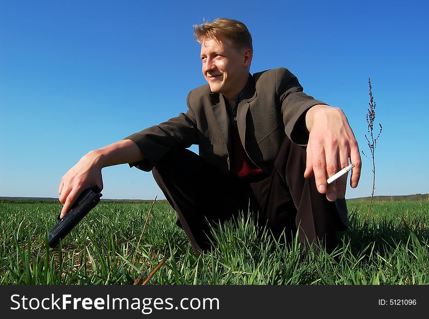 Young man squatting, with a gun and a cigarette, in a middle of a field. Young man squatting, with a gun and a cigarette, in a middle of a field