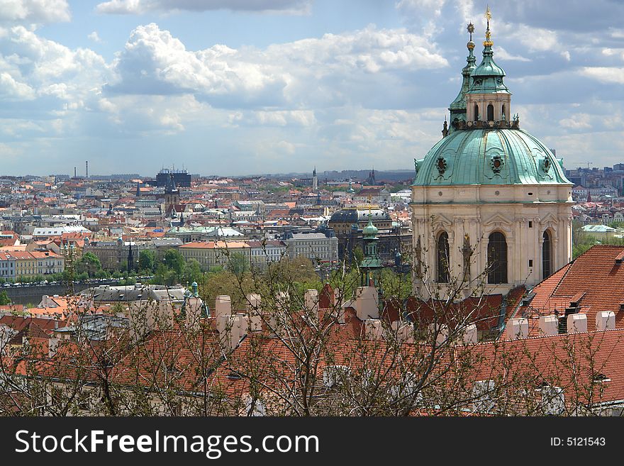 The Prague landscape with roofs of historical buildings. Top of an old cathedral at the right , tree branches Ð± clouds and sky . The Prague landscape with roofs of historical buildings. Top of an old cathedral at the right , tree branches Ð± clouds and sky .