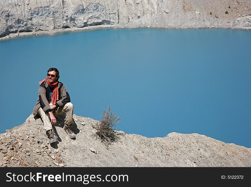 Trekker sitting on mountain summit with blue lake in background