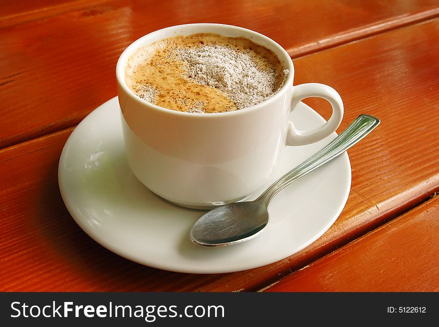 Cappuccino cup with metal spoon on wood background