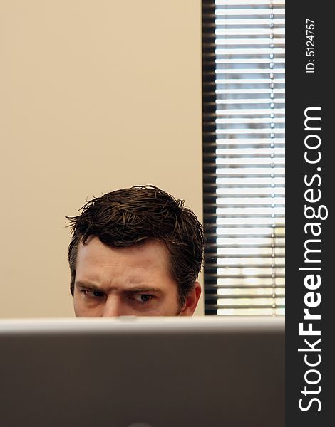 Businessman sitting behind his laptop with an angry look on his face. Vertically framed shot. Businessman sitting behind his laptop with an angry look on his face. Vertically framed shot.