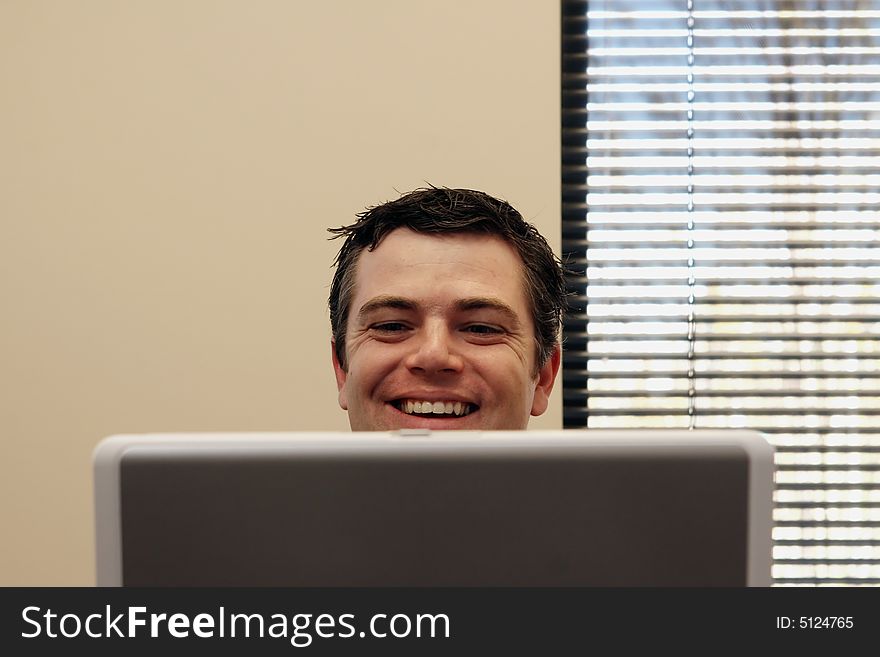 Businessman sitting behind a laptop screen with a broad smile on his face. Horizontally framed shot. Businessman sitting behind a laptop screen with a broad smile on his face. Horizontally framed shot
