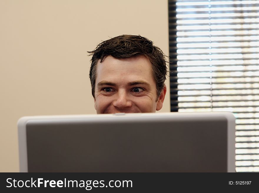Businessman sitting behind a laptop smiling as he reads the screen. Horizontally framed shot. Businessman sitting behind a laptop smiling as he reads the screen. Horizontally framed shot.