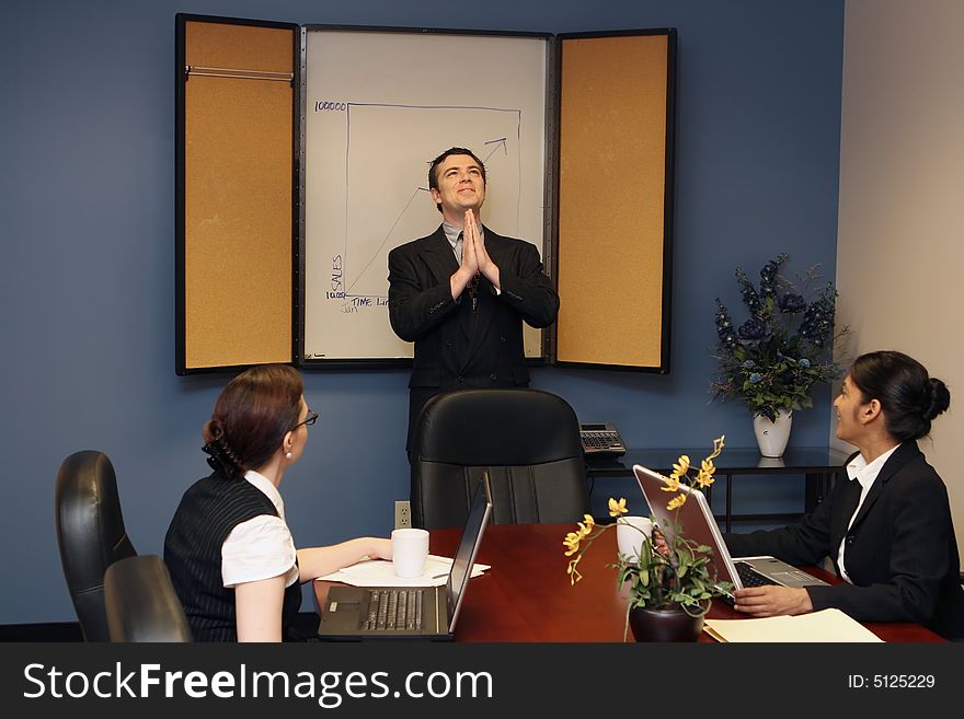 Businessman presenting to his colleagues staring up at the ceiling with his hands joined in prayer. Businessman presenting to his colleagues staring up at the ceiling with his hands joined in prayer