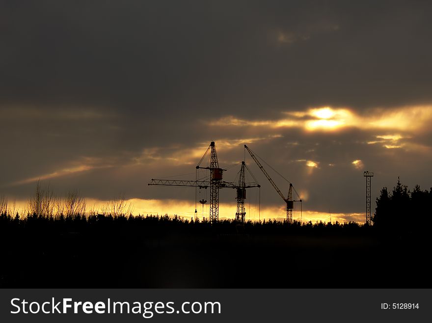 Cranes on a construction yard lightened by dawning sun. Cranes on a construction yard lightened by dawning sun