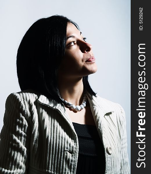 A high-key portrait about a young pretty woman with black hair who is looking up and she is dreaming. She is wearing a white coat, a black dress and a white necklace. A high-key portrait about a young pretty woman with black hair who is looking up and she is dreaming. She is wearing a white coat, a black dress and a white necklace.