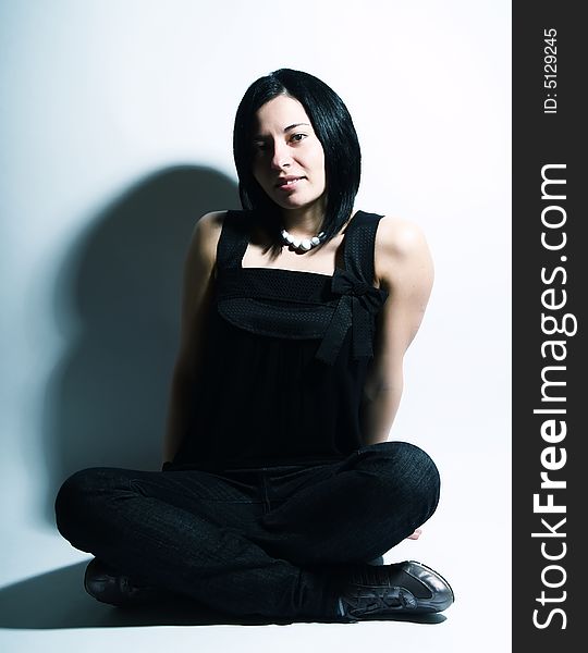 A portrait about an attractive trendy girl with black hair who is sitting and she has a charming look. She is wearing a black dress, blue jeans and a white necklace. A portrait about an attractive trendy girl with black hair who is sitting and she has a charming look. She is wearing a black dress, blue jeans and a white necklace.