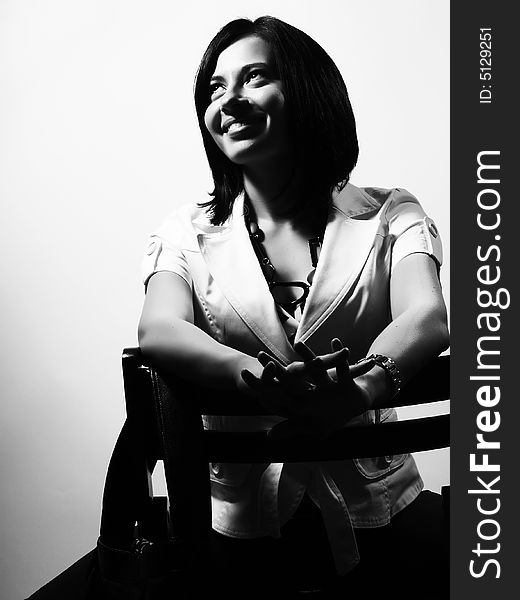 A black and white high-key portrait about a pretty trendy lady with black hair who is sitting on a chair, she is looking up and she is smiling. She is wearing a white coat and a stylish necklace. A black and white high-key portrait about a pretty trendy lady with black hair who is sitting on a chair, she is looking up and she is smiling. She is wearing a white coat and a stylish necklace.