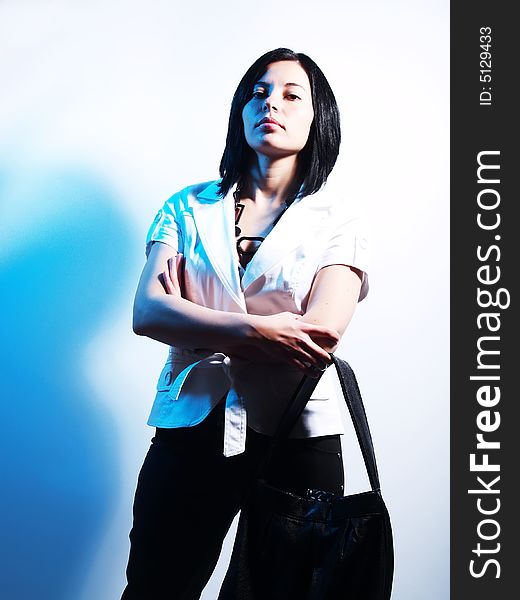 A high-key portrait about an attractive trendy lady with black hair who is lighted with blue and she has a charming look. She is wearing black pants, a white coat, a black necklace and a stylish handbag. A high-key portrait about an attractive trendy lady with black hair who is lighted with blue and she has a charming look. She is wearing black pants, a white coat, a black necklace and a stylish handbag.