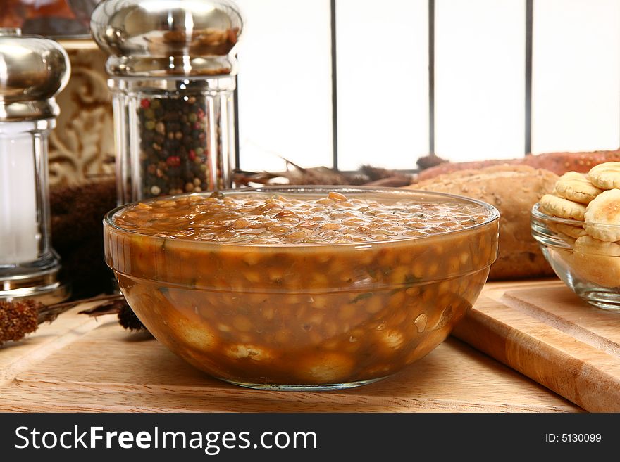 Bowl of hot lentil soup in glass bowl over bed of oyster crackers in kitchen or restaurant. Bowl of hot lentil soup in glass bowl over bed of oyster crackers in kitchen or restaurant.