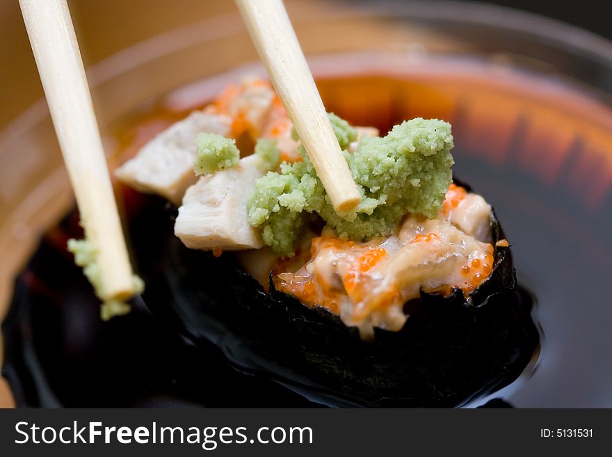 Taking sushi with chicken and wasabi from plastic saucer with chopsticks. Taking sushi with chicken and wasabi from plastic saucer with chopsticks