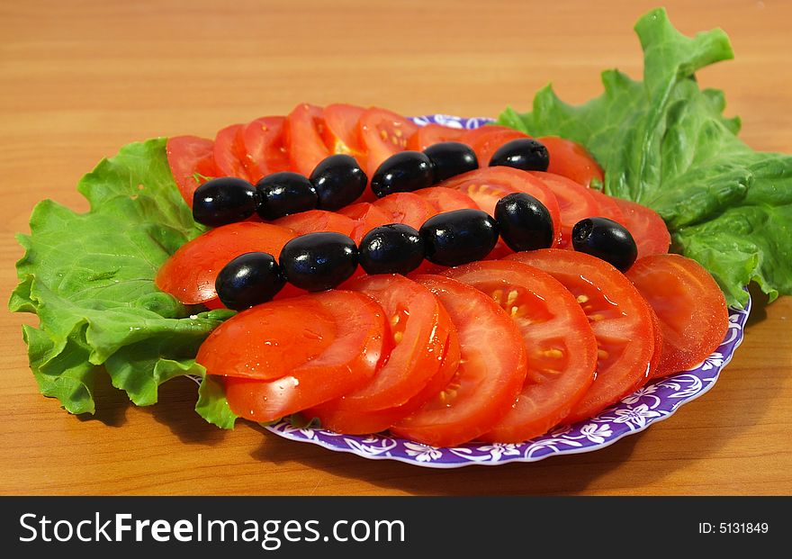 Tomatoes, leaves of salad and olives on a round plate. Tomatoes, leaves of salad and olives on a round plate