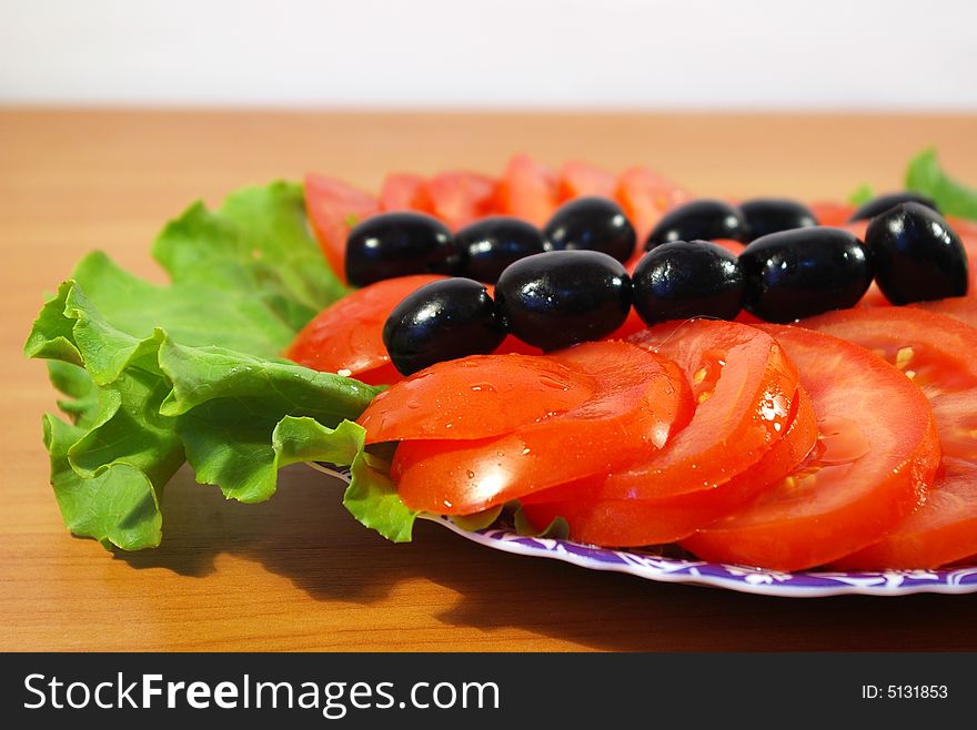 Tomatoes, leaves of salad and olives on a round plate. Tomatoes, leaves of salad and olives on a round plate