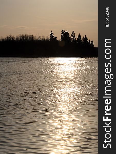 The evening sun shimmering on the water of a calm lake at sunset. The evening sun shimmering on the water of a calm lake at sunset
