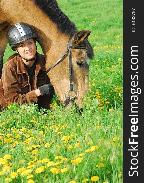 Woman kneeling in green field with yellow dandelions next to her horse. Woman kneeling in green field with yellow dandelions next to her horse.