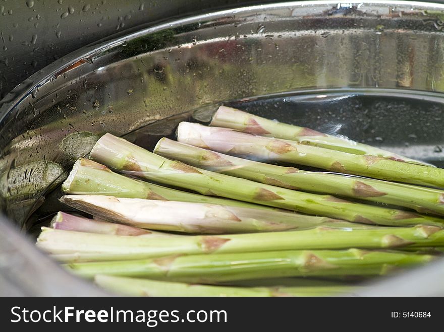 A bunch of asparagus soaking in a stainless steel bowl full of water.