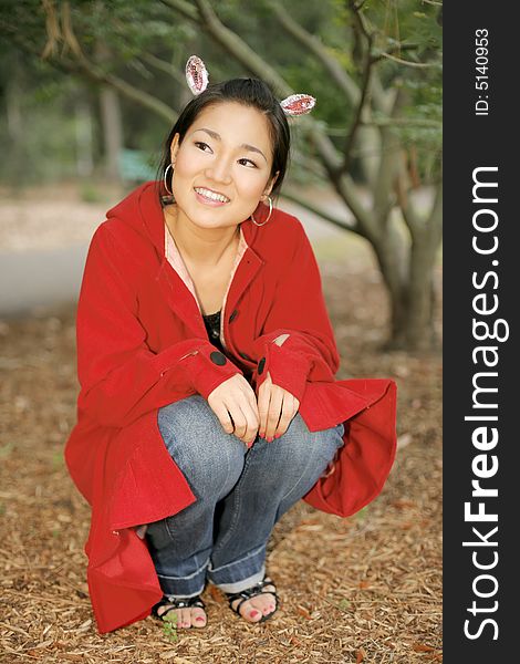 A pretty young Asian girl crouched in the woods with bunny ears on. A pretty young Asian girl crouched in the woods with bunny ears on