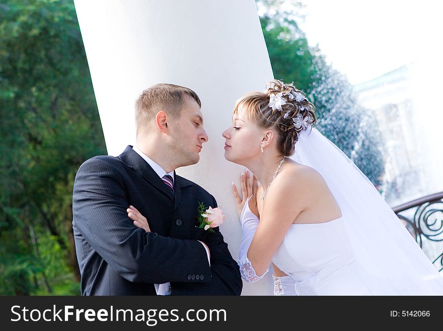 A bride and a groom stand by a white column and kiss. A bride and a groom stand by a white column and kiss