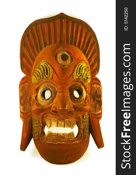 A wooden mask painted brick red and sage green, with fierce teeth and a third eye.  A crown surmounts the grimacing face. A wooden mask painted brick red and sage green, with fierce teeth and a third eye.  A crown surmounts the grimacing face.