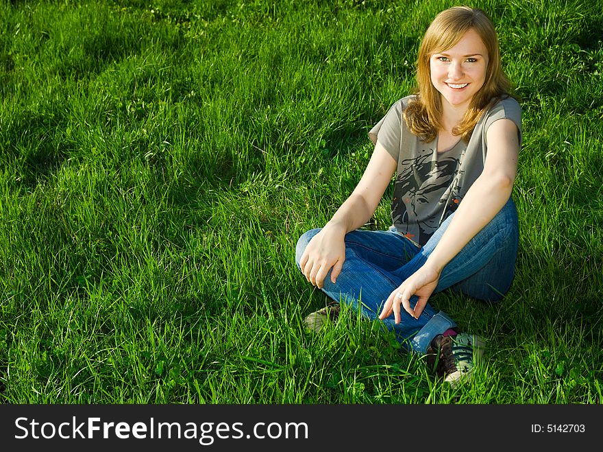 Beautiful and happy young woman with toothy smile, sitting on the grass, with copy space. Beautiful and happy young woman with toothy smile, sitting on the grass, with copy space