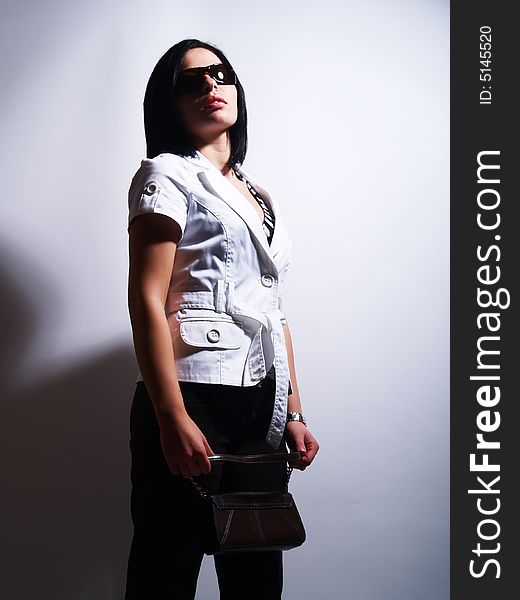 A high-key portrait about a pretty trendy lady with black hair who has an attractive look. She is wearing sunglasses, black pants, a white coat and a stylish purse. A high-key portrait about a pretty trendy lady with black hair who has an attractive look. She is wearing sunglasses, black pants, a white coat and a stylish purse.