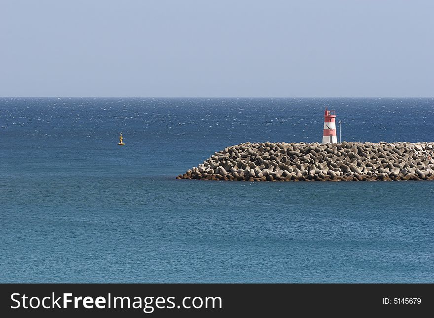 Little lightouse at an harbor entrance, isolated in blue sky