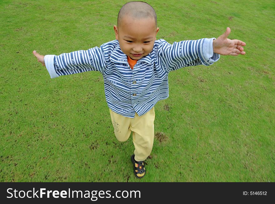 A Chinese little boy run happily on the green meadow. A Chinese little boy run happily on the green meadow.