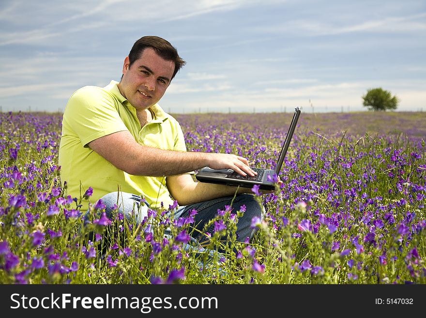 Young man with laptop computer on a flower field