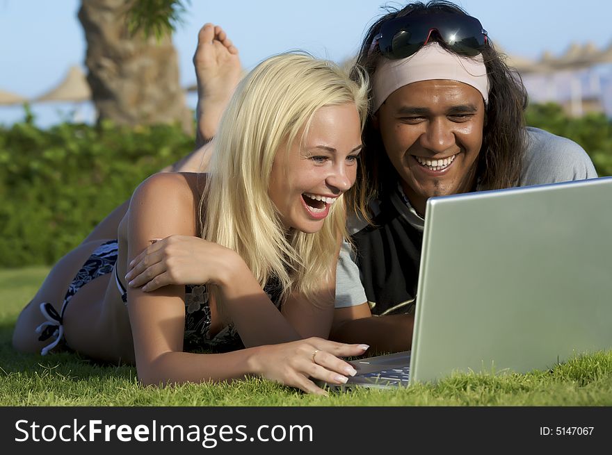 Young multi-ethnic couple lay on grass with laptop. Young multi-ethnic couple lay on grass with laptop.