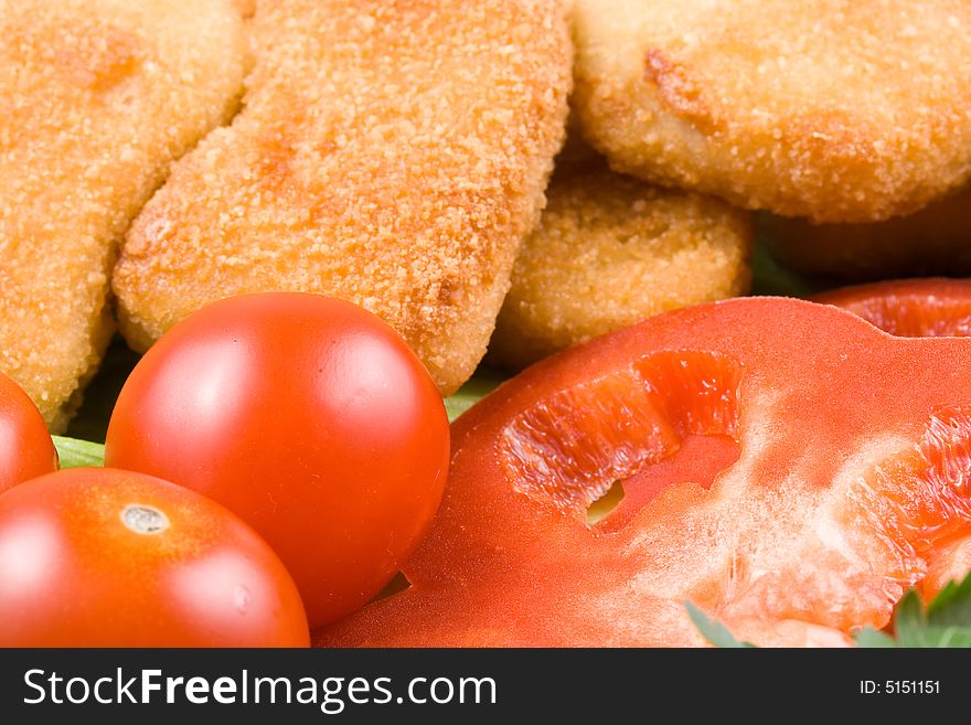 Appetizing fried chicken nuggets with tomatoes, cucumber and pepper on salad leaves. Close-up. Selective focus. Appetizing fried chicken nuggets with tomatoes, cucumber and pepper on salad leaves. Close-up. Selective focus.