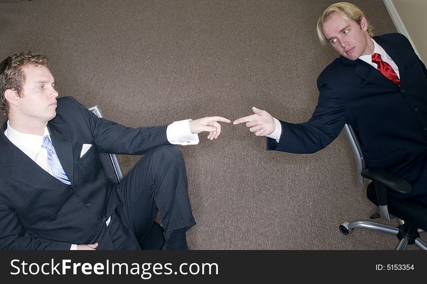 Two businessmen in suits sitting down in office turning to touch fingers. Two businessmen in suits sitting down in office turning to touch fingers