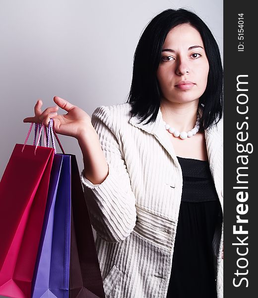 A high-key portrait about a pretty trendy lady with black hair who is holding some shopping bags and she has an attractive look. She is wearing a white coat, a black dress and a white necklace. A high-key portrait about a pretty trendy lady with black hair who is holding some shopping bags and she has an attractive look. She is wearing a white coat, a black dress and a white necklace.