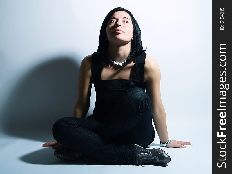 A portrait about an attractive trendy girl with black hair who is sitting, she is spreading her arms on ground, she is looking up and she is admiring something. She is wearing a black dress, blue jeans and a white necklace. A portrait about an attractive trendy girl with black hair who is sitting, she is spreading her arms on ground, she is looking up and she is admiring something. She is wearing a black dress, blue jeans and a white necklace.