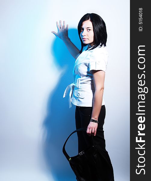 A high-key portrait about a cute trendy lady with black hair who is leaning against the wall and she has an attractive look. She is wearing black pants, a white coat and a stylish handbag. A high-key portrait about a cute trendy lady with black hair who is leaning against the wall and she has an attractive look. She is wearing black pants, a white coat and a stylish handbag.