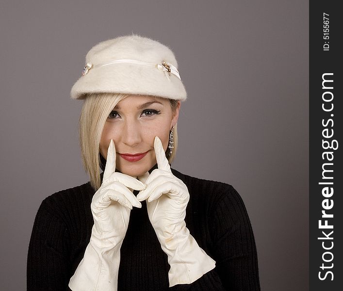 A blonde in black turtleneck and white fur hat with white gloves holding her smile with two fingers. A blonde in black turtleneck and white fur hat with white gloves holding her smile with two fingers