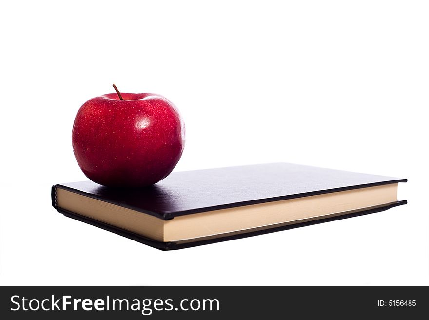 A black school book and a red apple on a white background with copy space. A black school book and a red apple on a white background with copy space