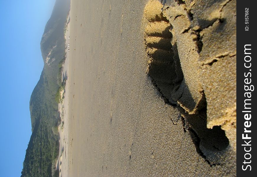 A footprint in the sand at the beach with mountains in the back-round