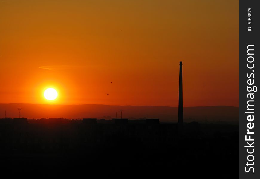 Skyline at sunset with a smoke-stack