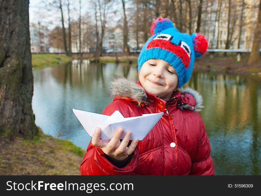 Little girl holding a paper boat near the river