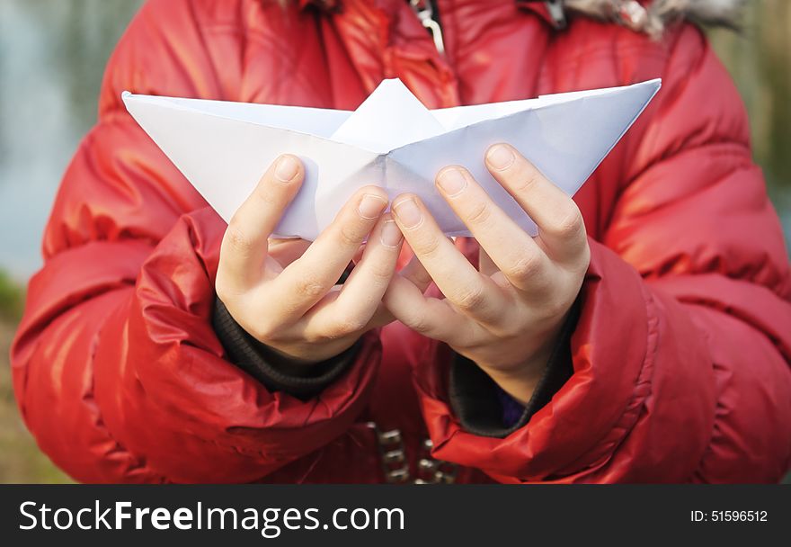 Hands holding a paper boat closeup outside